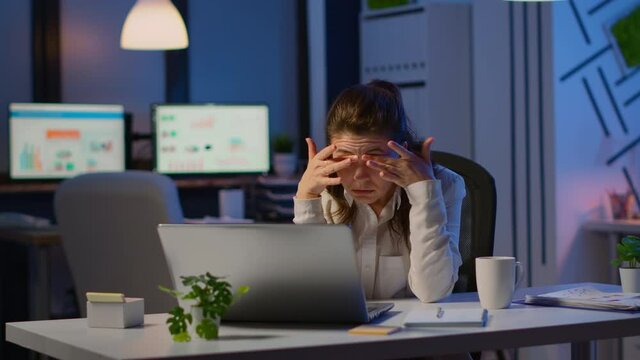 Stressed businesswoman suffering from headache at work doing overtime late night. Exhausted tensed worker coping with migraine, emotional stress concept feeling pain sitting at office desk with laptop