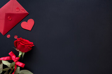 Valentines day background. Red flowers of rose and envelop with heart on black background, top view, copy space