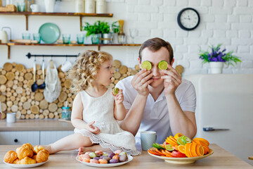 Happy family autey and daughter in the kitchen. Parenting is a game. Choose between fruit or cookies. The concept of healthy eating.
