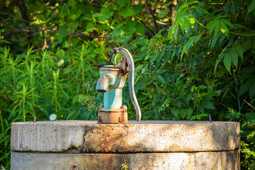 An old, rusty hand pump well in the forest. Still works and water still drinkable.