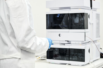 Scientist in rubber gloves and white lab coat standing near high performance liquid chromatography...
