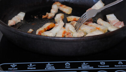 Fried pieces of bacon in a black pan.Pork belly close-up.