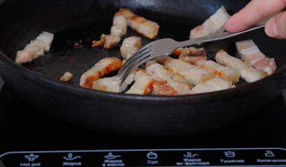 Fried pieces of bacon in a black pan.Pork belly close-up.