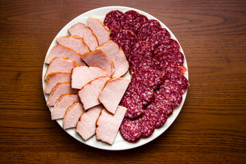 Sausage and meat cuts on a white plate on a wooden table. Fresh meat products