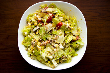 Salad with cabbage, ham, cheese and cherry tomatoes on a white plate. Against the background of a wooden table. Homemade food. Snack