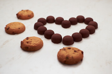Valentine's Day. Heart made of chocolates and cookies on a white background with lights