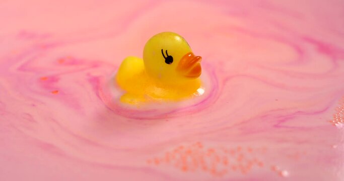 Cute yellow duck toy floats in a pink colourful foam closeup.