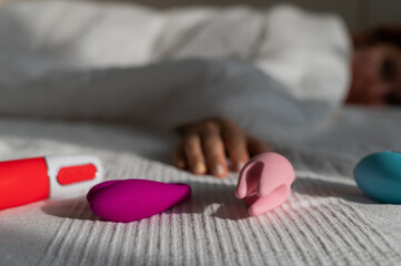 The woman lies in bed under a white blanket and reaches for the vibrators. Girl and sex toys in the...
