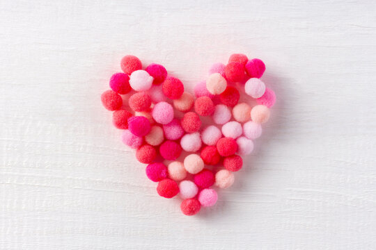 Soft heart made of small wool pompons as a sign of gentle love on white wood table