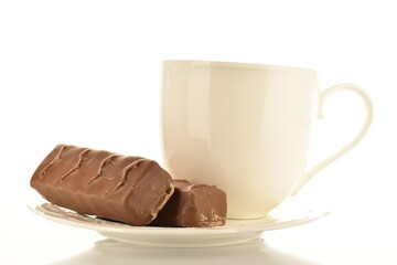Two sweet chocolate bars with ceramic white cup and saucer, close-up, isolated on white.