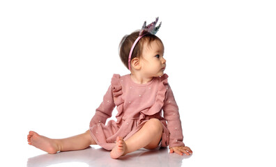 little cute baby in a headband in the form of a crown sits in a pink dress on a gray background, looks to the side at an empty seat. dad and mom princess
