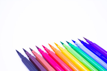 Multi-colored markers with a brush tip, arranged according to the colors of the rainbow. White background. The concept of creativity, drawing, bright world, back to school, study. Copy space