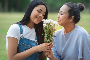 Obraz premium Asian teenager daughter gives her bouquet of flowers to her mother at park, Happy mother's day