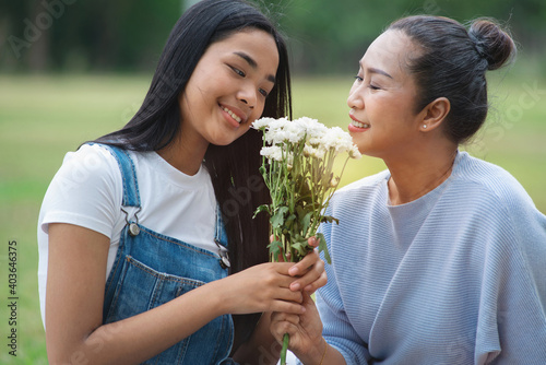 Asian teenager daughter gives her bouquet of flowers  to her mother at park, Happy mother's day