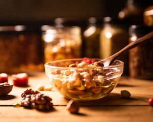 Farmer Honey mixed with nuts, seeds in a transparent plate with a wooden spoon, jars, walnuts, dried apricots and a branch of red rowan on a rustic wooden kitchen table. Still life photography