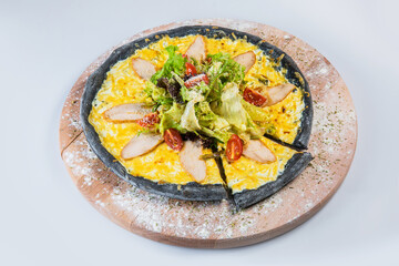 Whole meat black dough Pizza in Caesar salad style on wooden plate, isolated on gray background. Pizza With grilled chicken slices, bacon, fresh lettuce, cherry tomatoes served with parmesan cheese