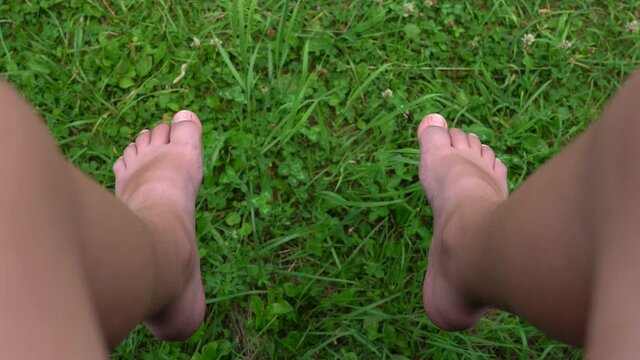 Point of view 4k video of two funny male barefeet legs of young teenage kid of 13 years old isolated on green grass background