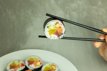 Hand holding sushi roll using chopsticks on gray background