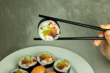 Hand holding sushi roll using chopsticks on gray background