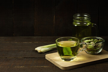 Lemon grass tea in glass and fresh lemon grass on wooden background. Healthy herbal drink concept dark tone.