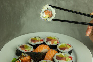 Hand holding sushi roll using chopsticks on gray background