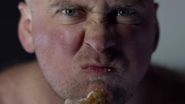 Hungry, angry and angry man eating fried chicken leg in breadcrumbs, close-up face with bulging eyes, Fast food concept.