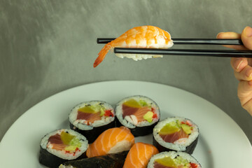 Hand holding sushi roll using chopsticks on gray background
