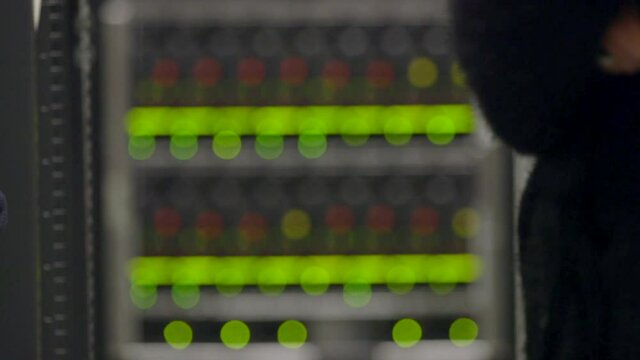 Green blinking lights on computer data storage. Soft focus bokeh. Man walks past in foreground