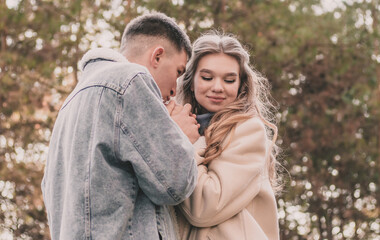 the guy holds the girl's hands and kisses them and the girl smiles while in the pine forest in winter