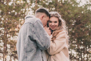 Obraz premium the guy holds the girl's hands and kisses them and the girl smiles while in the pine forest in winter