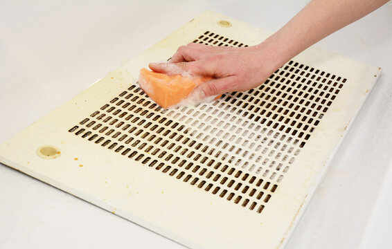 Regular Kitchen Exhaust Hood Cleaning: A Woman Is Cleaning A Greasy And Dusty Metal Grate Filter From A Kitchen Range Hood, Extraction Hood, Cooker Hood Using Hot Water, Dish Soap And A Sponge.