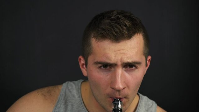 man smokes vape and smokes into the camera on a black background
