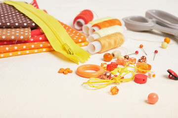 spools of thread, scissors, fabrics, a zipper and accessories for sewing and needlework on the table, beads, buttons and pins