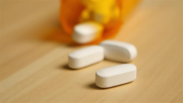 Zooming up to a spilt bottle of white prescription pill tablets on a wooden tabletop