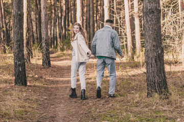 
the guy hugs the girl tightly and kisses her on the cheek while in the pine forest