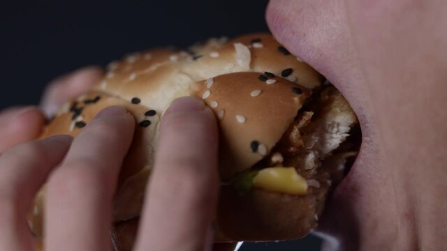 Middle-aged woman eating a hamburger. Close-up of the mouth in profile. Fast food. Burger in the women's hands.