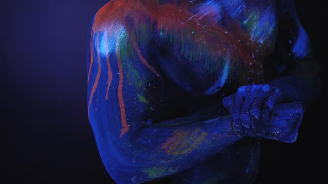 Close-up of the naked chest of a muscular man with ultraviolet drawings on the body in the light of fluorescent lamps.