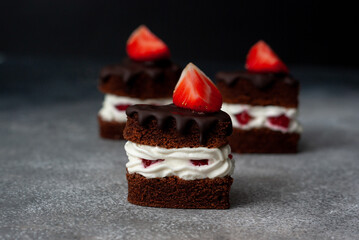 Three pieces of chocolate strawberry layered cake with white cream on dark grey background