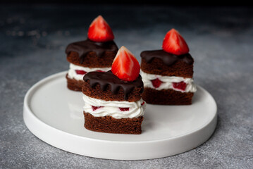 Three pieces of chocolate strawberry layered cake with white cream on dark grey background
