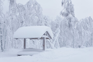 wooden gazebo with picnic table in a snowdrift after a heavy snowfall in a frosty winter park