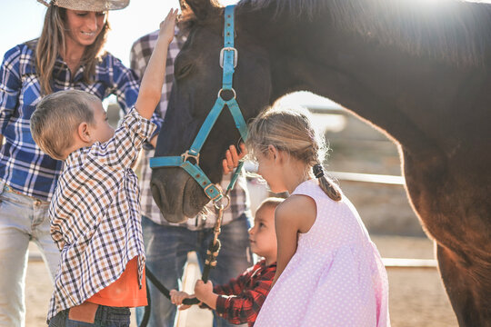 Cheerful family enjoy day outdoor at ranch while the children cuddle a horse - Human and animal love - Powered by Adobe