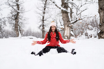 Fototapeta na wymiar Young brunette woman in red sweater playing with snow in park