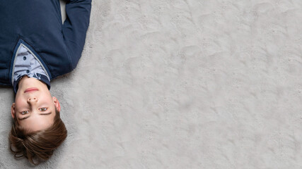 Teens boy lie on grey carpet, copy space