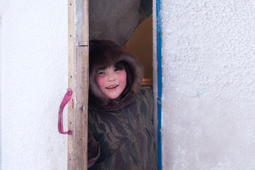 Young girl, in the national winter clothes of the northern inhabitants of the tundra, the Arctic circle, girl looking out the door of the house