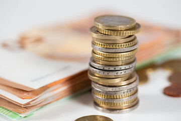 Coins lying on the table with banknotes blurred in the background. Euro money stacked in column on white desk. Concept of wealth and financial success.