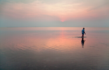 Lake Syvash at sunset,  a man walking in the reflection of the pink sky.