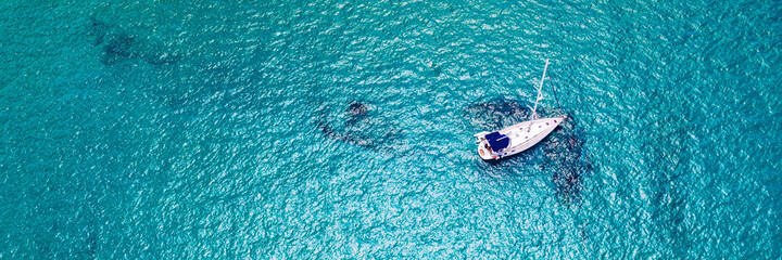 Yacht anchoring in crystal clear turquoise water in front of the tropical island, alternative lifestyle, living on a boat. Aerial view of yacht at anchor on turquoise water, showing luxury, wealth. © daliu
