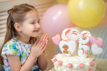 Fototapeta na wymiar Happy Birthday Smiling little girl makes a wish, next to the birthday cake.