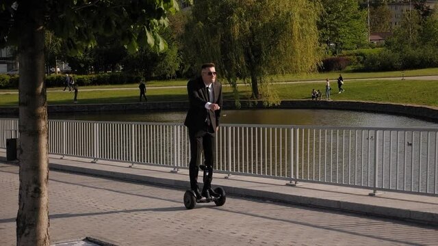 A cheerful man in a suit rides a gyro scooter in the Park, he has fun and simulates a slow run. A happy businessman is having fun with a gyro scooter. Slow motion.