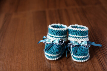 Fototapeta na wymiar Comfortable hand-knitted children's shoes on wooden background. Crocheted booties for newborns. preparation for birth and Motherhood